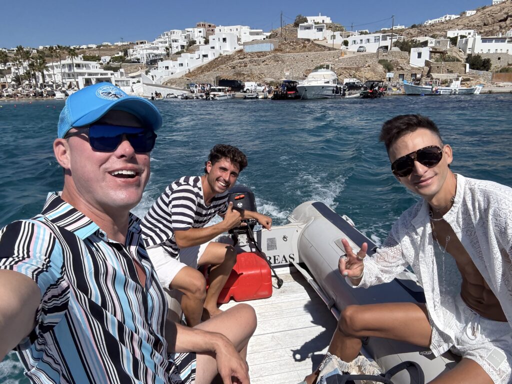 Chris and his husband CK riding a tender boat in Ornos Bay, Mykonos, on the way to their private yacht during a Pride Adventures LGBTQ+ travel experience.