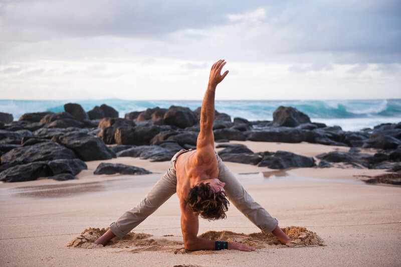 Man stretching on the beach in Hawaii, representing yoga and mindfulness sessions during the CGA Hawaiian Weekend Getaway
