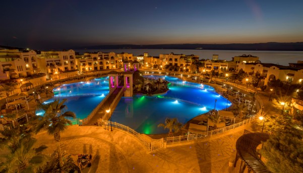 Aerial night view of the Crowne Plaza Dead Sea Resort in Jordan with illuminated pools overlooking the shoreline and desert landscape