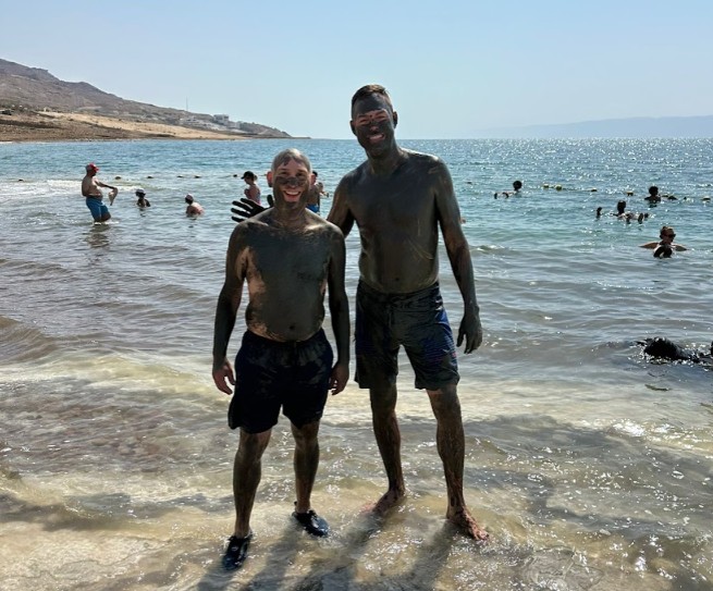 Chris Smith and another traveler covered in Dead Sea mud along the shoreline of the Dead Sea in Jordan