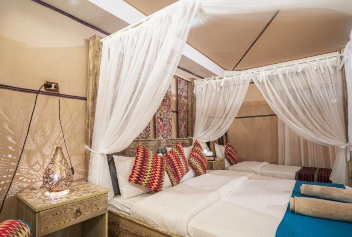 Shared room in a Bedouin style desert camp in Wadi Rum Jordan with canopy beds colorful cushions and soft lantern lighting