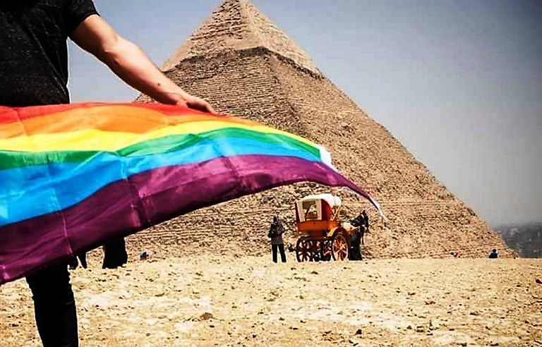 Traveler holding a rainbow Pride flag near the Pyramids of Giza in Egypt, symbolizing LGBTQ+ travel and cultural connection on the Pride Adventures Egypt & the Nile journey.