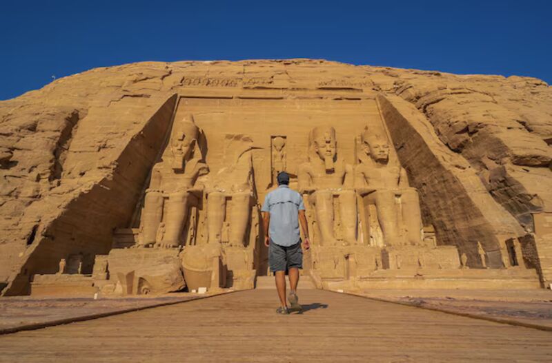 Traveler walking toward the Abu Simbel temples in Egypt under clear desert skies.