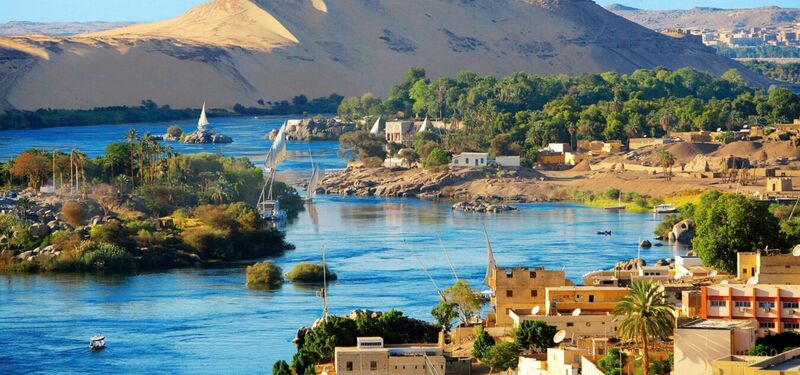 Panoramic view of the Nile River flowing through Egypt with golden desert hills and palm trees, featured in the Pride Adventures LGBTQ+ Egypt & the Nile group trip.