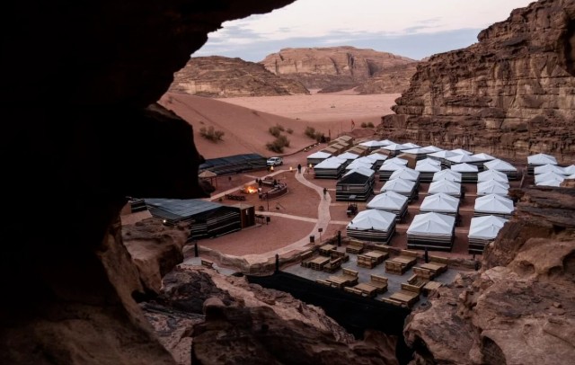 View from a cave in the sandstone cliffs overlooking a Bedouin desert camp in Wadi Rum Jordan with tents and red sand landscape