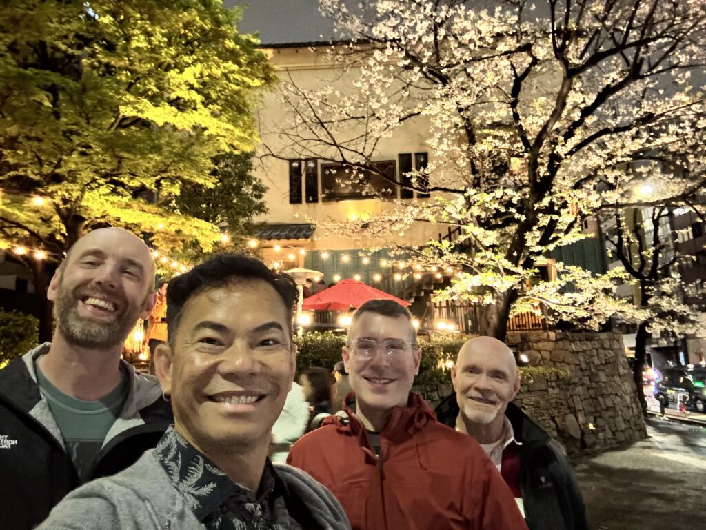 LGBTQ+ travel friends laughing under illuminated cherry blossoms at night in Kyoto Japan