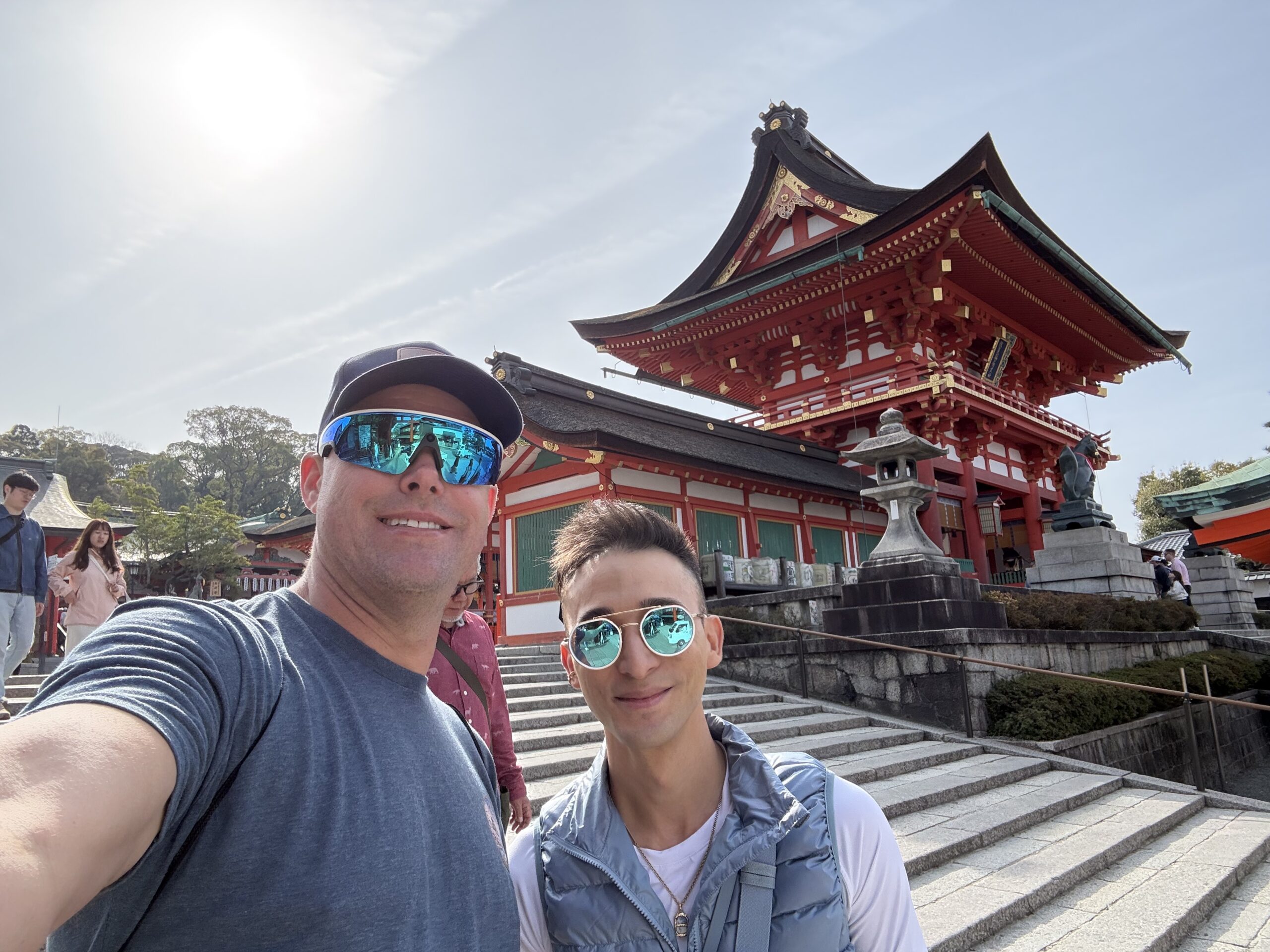 Couple selfie in front of a red Japanese shrine gate with cherry blossoms in Kyoto Japan