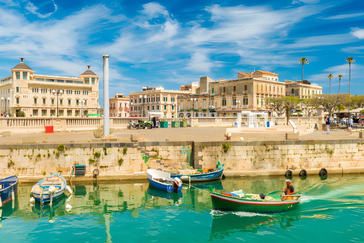 Colorful fishing boats in turquoise harbor waters along the waterfront promenade of Syracuse Ortigia island Sicily on Pride Adventures LGBTQ+ tour