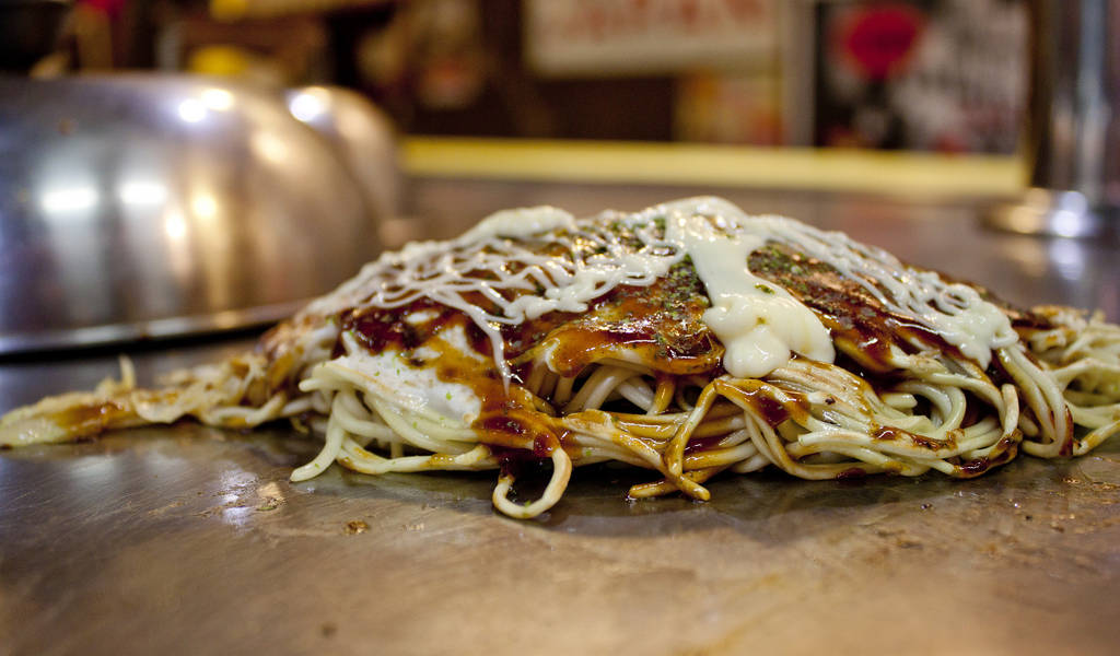 Hiroshima-style okonomiyaki savory pancake being cooked on a hot iron griddle in Japan