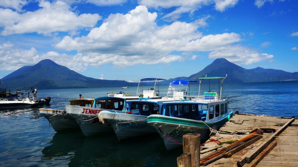 Colorful wooden boats docked on Lake Atitlán with three towering volcanoes rising in the background, Guatemala