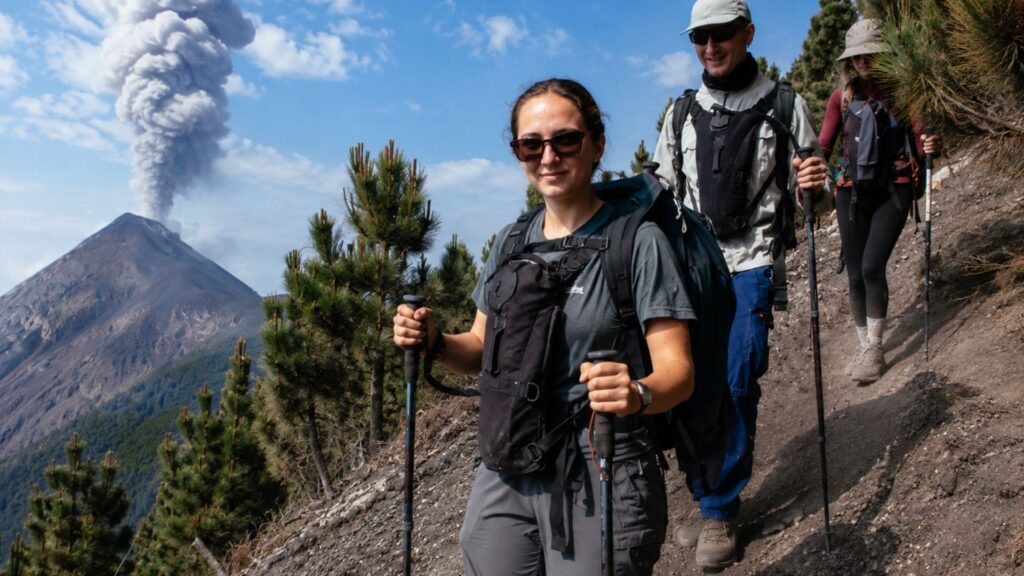 Two hikers with backpacks and trekking poles on a volcano trail in Guatemala with an active volcano in the background