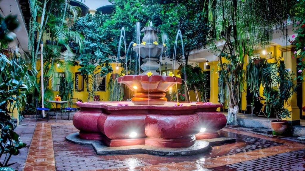 Illuminated colonial courtyard fountain surrounded by tropical plants at Hotel Posada San Vicente in Antigua, Guatemala