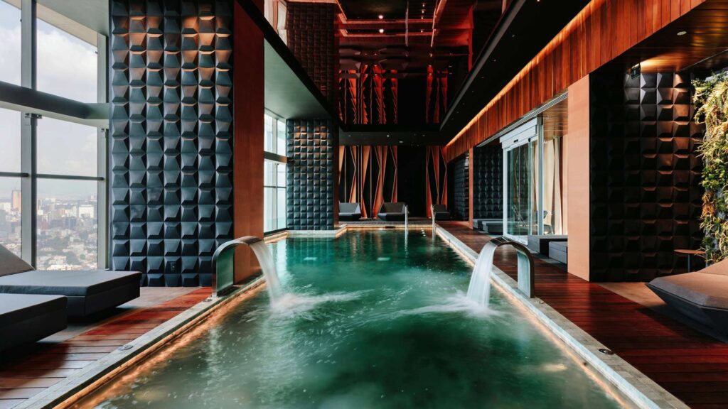 Dramatic indoor pool at the Sofitel Mexico City with geometric wall panels, wood ceiling, city views, and a waterfall feature