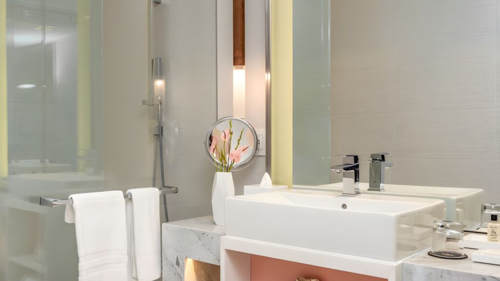 Elegant marble and white Sofitel Mexico City bathroom with vessel sink, chrome fixtures, glass shower, and flower arrangement