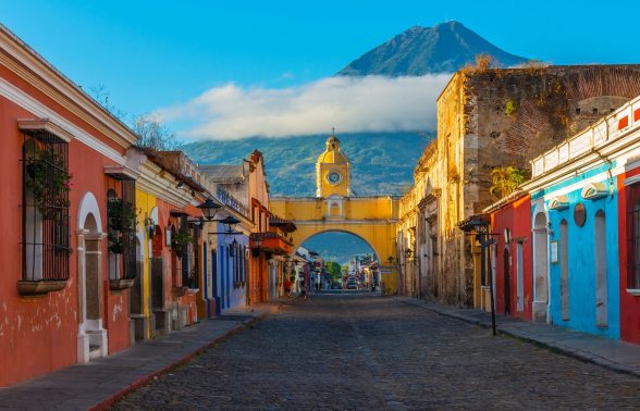 Antigua's iconic yellow Santa Catalina Arch framing a colorful colonial street with a volcano in the background