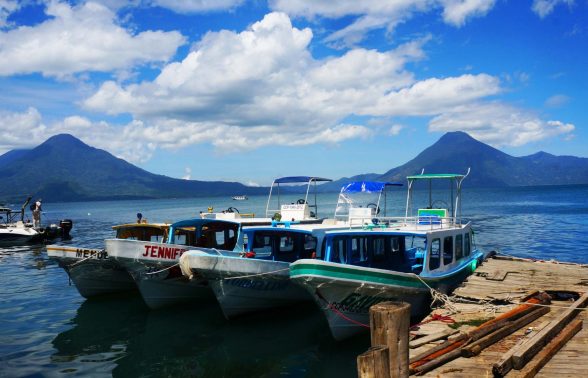 Colorful wooden boats docked on Lake Atitlán with three towering volcanoes rising in the background, Guatemala