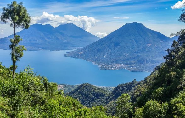 Panoramic view of Lake Atitlán surrounded by three towering volcanoes and lush green hills in Guatemala